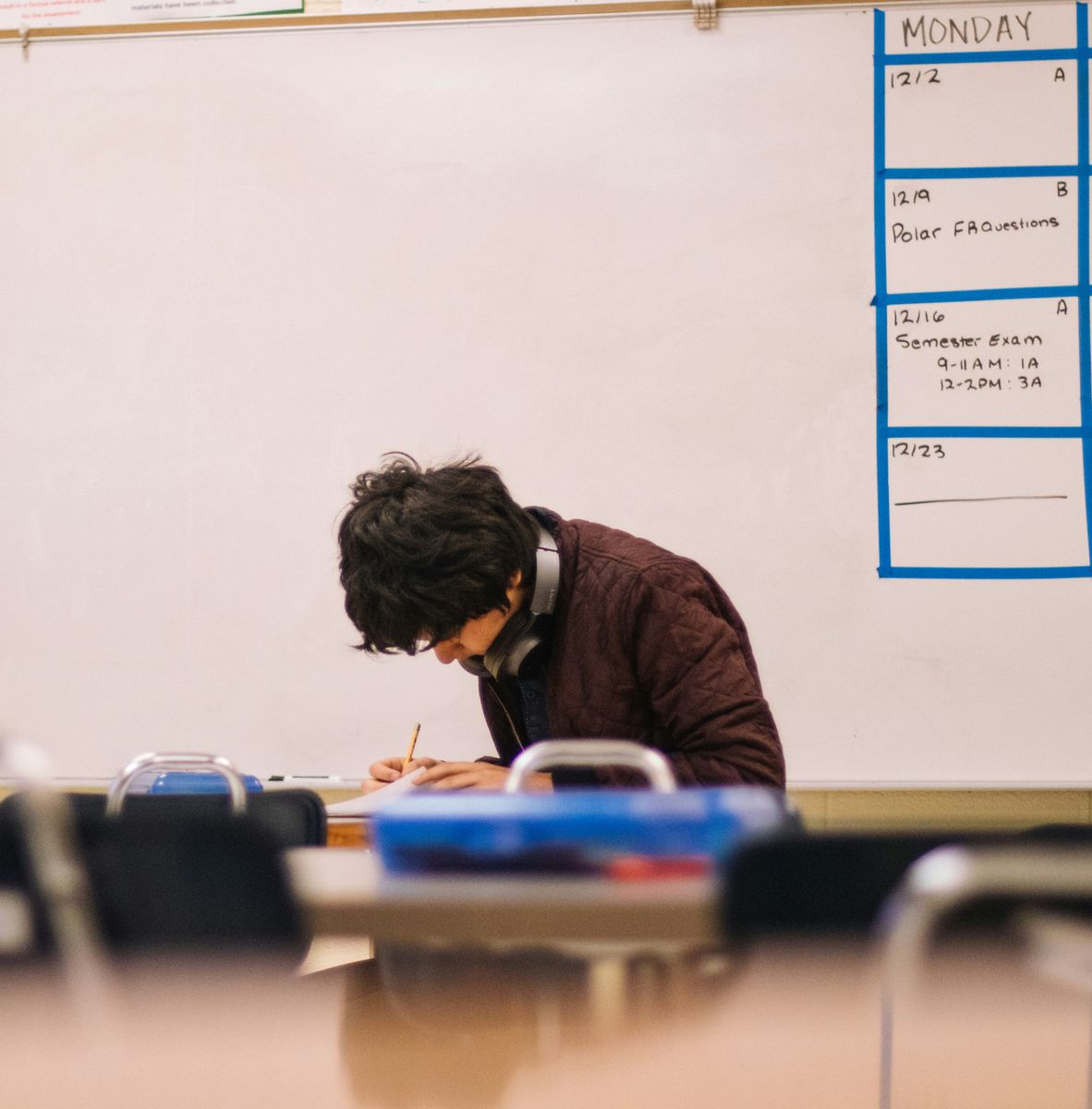 High school student bent over a classroom desk studying — neck and back pain care for students at High Amplitude Health San Mateo